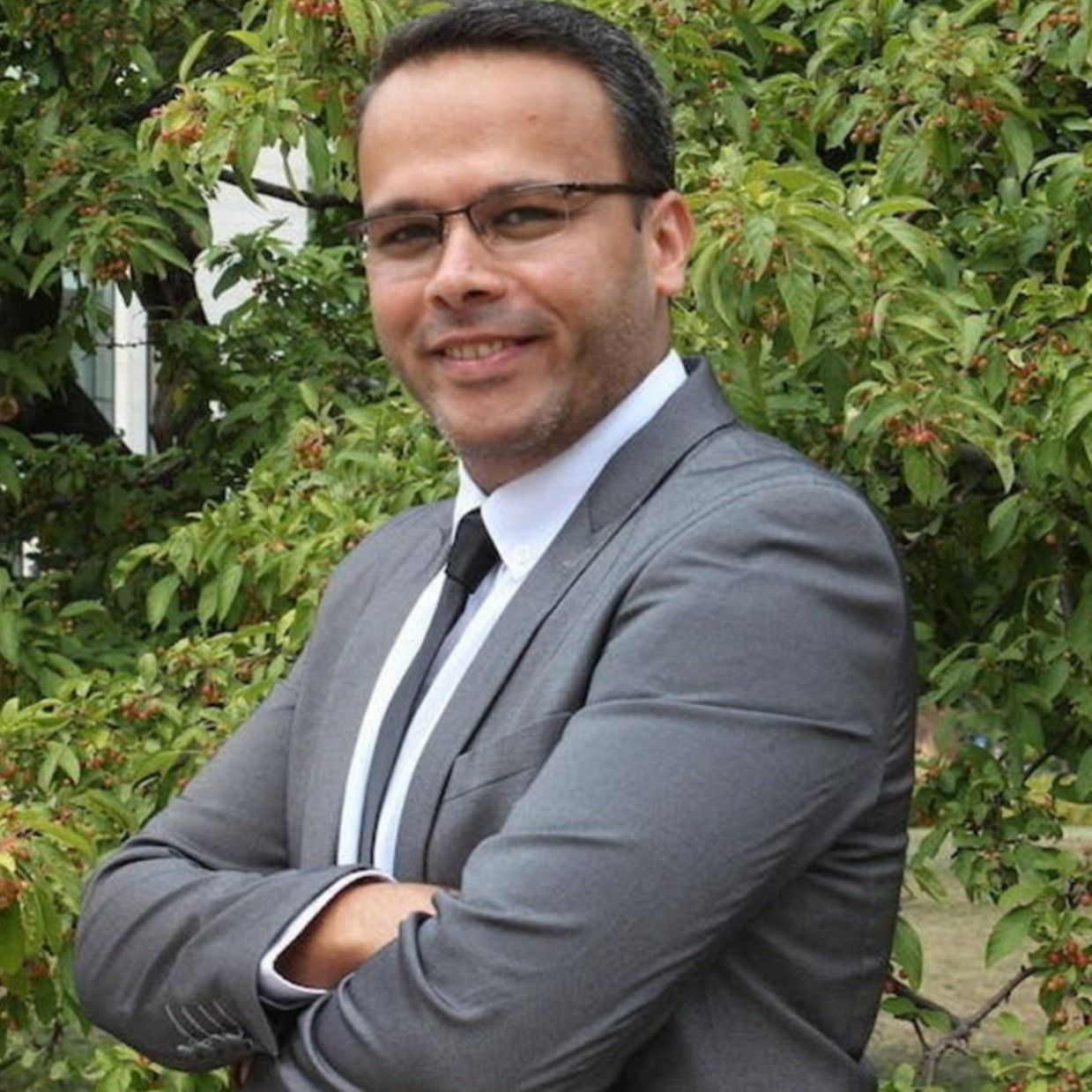 A man in a suit folds his arms and smiles for a photo