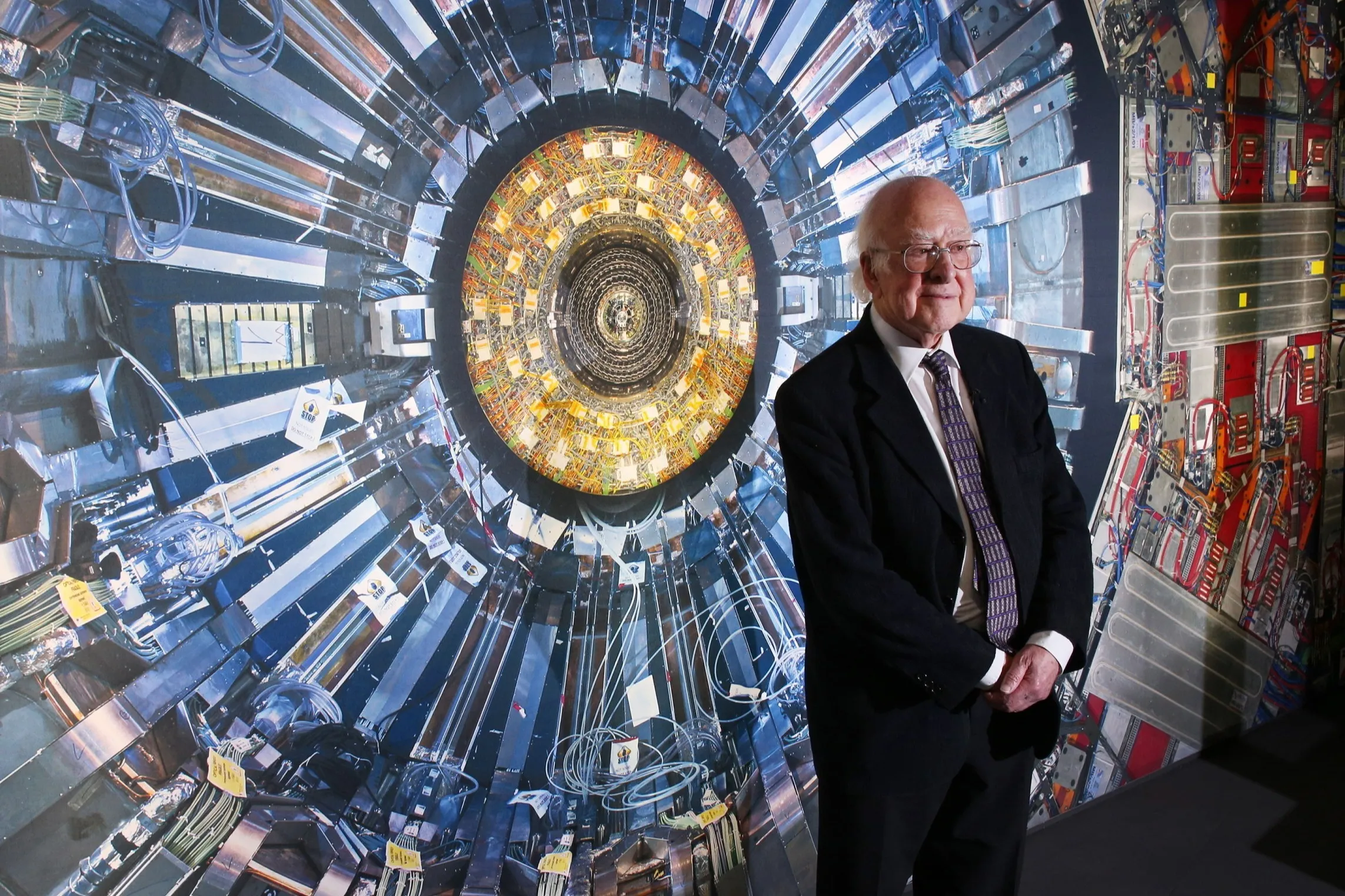 A man in a suit stands in front of a photograph of the Large Hadron Collider at the科學Museum 